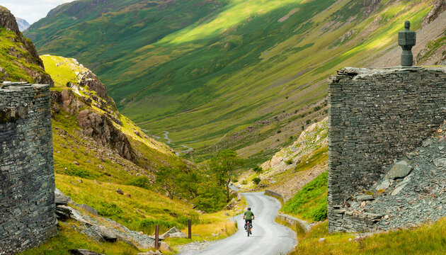 A bicycle rider peddles into Honister Pass,along a narrow,winding road,the Lake District,Cumbria,England,United Kingdom.