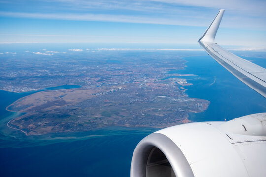 Airplane wing view above Copenhagen coastline over the Oresund sea strait during daytime flight travel
