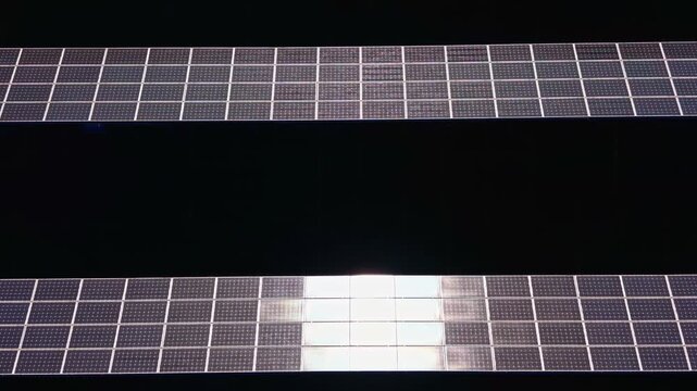 Solar panels are lined up in rows, reflecting sunlight. This setup demonstrates the use of renewable energy sources in a practical application during the day.