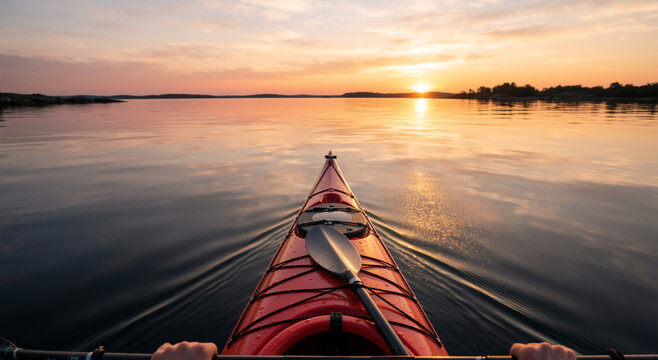 POV of red kayak on still water at sunset. First person perspective of kayaking during golden hour. Outdoor adventure and summer vacation concept