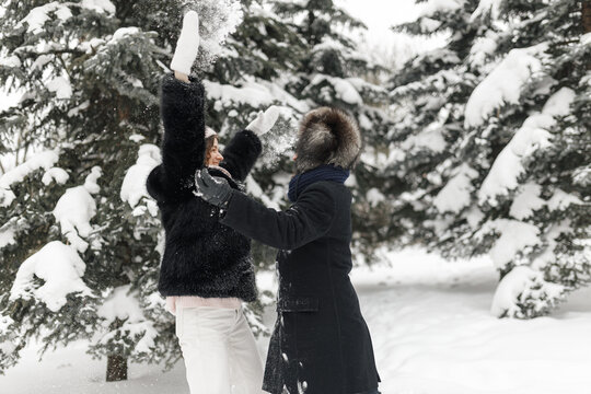 Side view of joyful boyfriend and girlfriend playing and having fun while throwing snow in winter forest 