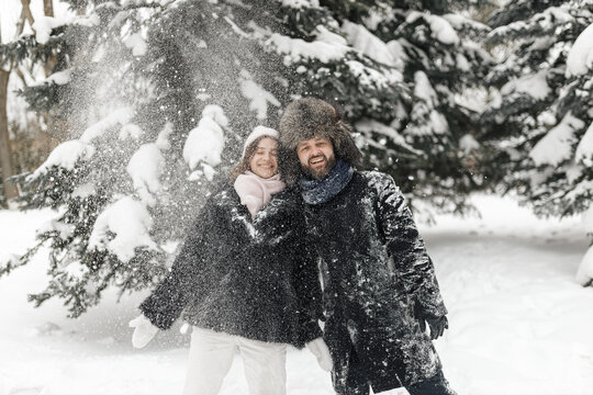 Portrait of happy beloved couple standing under snowfall in winter park in snowy weather and having fun 