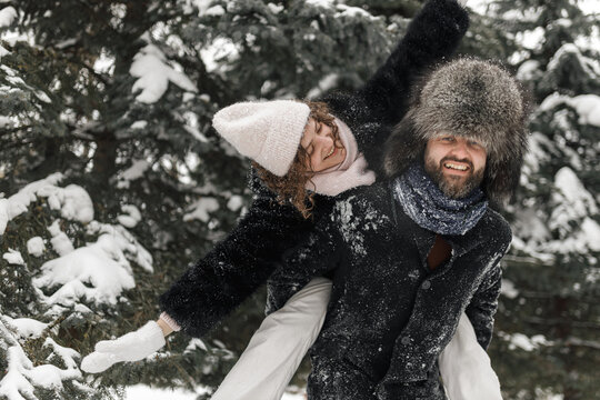 Smiling boyfriend giving piggyback ride to happy girlfriend in winter snowy park 