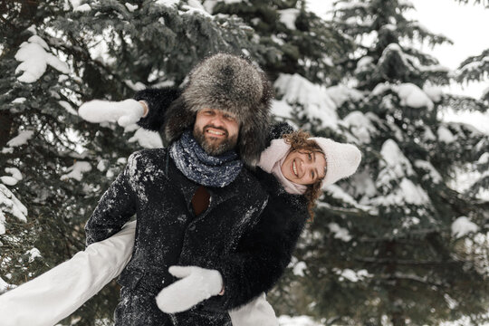 Happy couple having fun during piggyback ride in winter park and looking at camera 