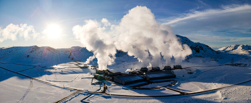 Aerial view of a geothermal power plant nestled in the stark, snowy landscape, juxtaposed against the billowing steam and distant mountains, Geothermal Power Plant, Sveitarfelagid Olfus, Iceland.