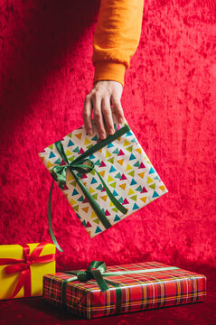 Hand holding a wrapped gift with bow above festive presents on red background