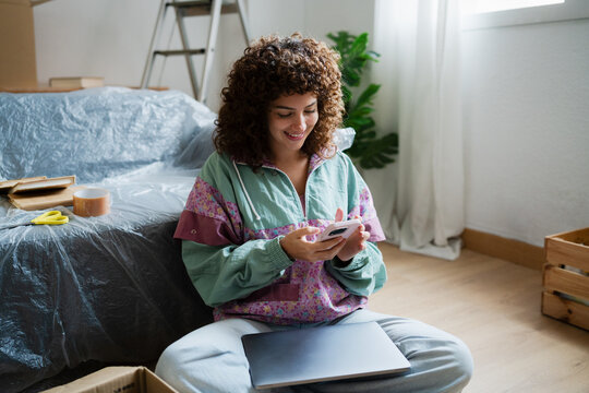Smiling woman using smartphone while sitting on floor at home