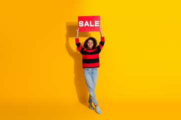 Fototapeta premium Young woman model holds sale sign against bright yellow background promoting discount shopping and fashion