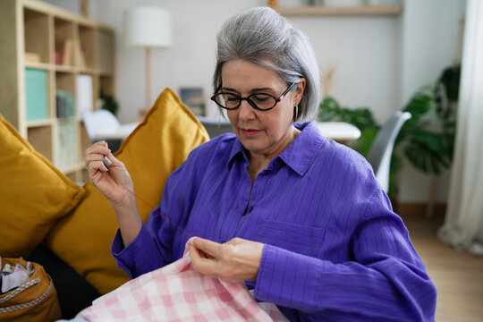 Woman sewing fabric at home in leisure sitting on an armchair