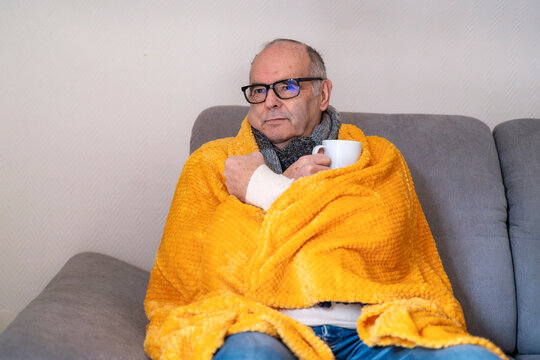 Man with blanket and hot drink on sofa during cold weather at home