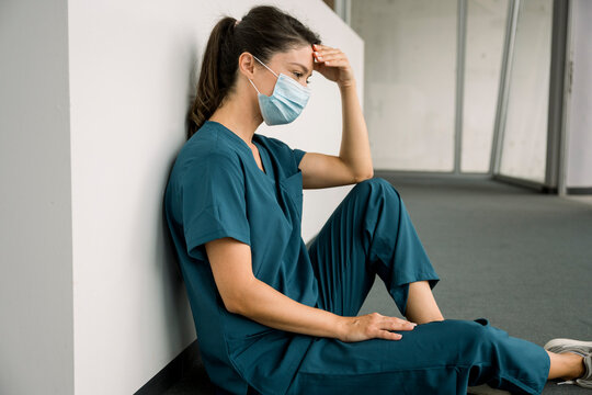 Nurse in scrubs sitting on hospital floor appearing exhausted