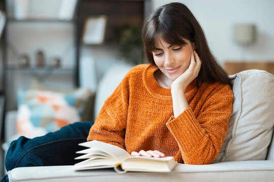Calm woman reading a book on a cozy couch indoors