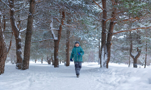 Boy laughing and running in snowy winter forest outdoors