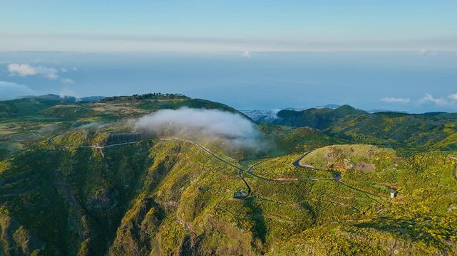 Mountain landscape with winding road and drifting cloud layer near Pico do Arieiro, Madeira Island, captured from drone at medium altitude