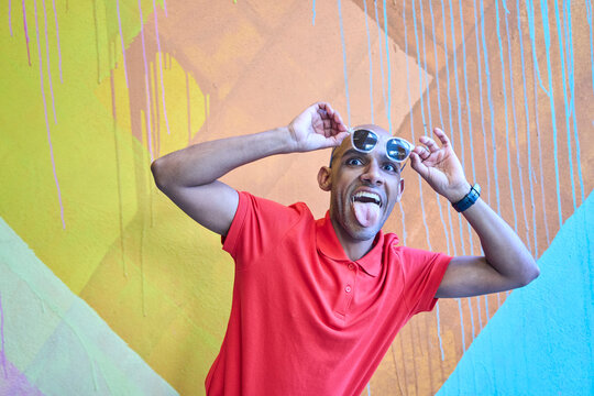 Playful man in red shirt posing with sunglasses against colorful mural