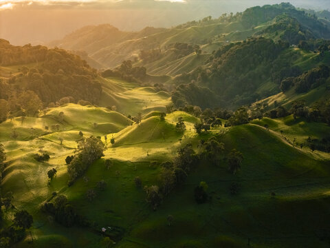 Aerial view of rolling hills kissed by a golden sunset, where vibrant green pastures meet the rugged terrain, Murillo, Tolima, Colombia.