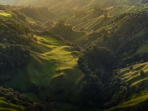Aerial view of rolling green hills and shadowed valleys create a tapestry of light and depth, a serene landscape bathed in golden sunlight, Murillo, Tolima, Colombia.