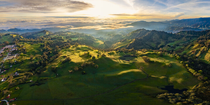 Aerial view of rolling hills blanketed in vibrant green hues, kissed by the golden light of dawn, casting long shadows across the landscape, Murillo, Tolima, Colombia.