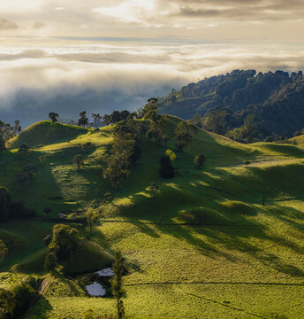 Aerial view of rolling green hills kissed by sunlight, where shadows dance and clouds linger, Murillo, Tolima, Colombia.