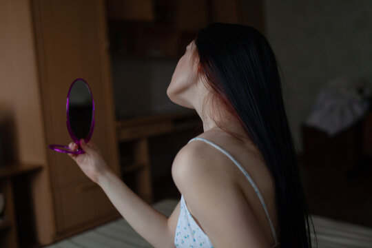 Woman with long hair sitting on bed at home holding a mirror