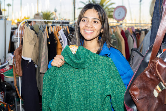 Smiling person shopping for a green sweater at flea market outdoors