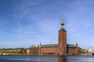 Obraz premium Stockholm City Hall viewed from Riddarholmen island, Sweden. Historic brick tower across the water under a clear blue sky