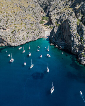Aerial view of turquoise waters meet rugged cliffs where boats bob gently near Torrent de Pareis, Mallorca, Balearic Islands, Spain.