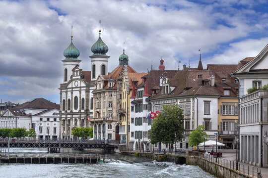 Jesuit Church and Reuss river with rushing water weir in Lucerne, Switzerland. Cloudy June sky in summer day