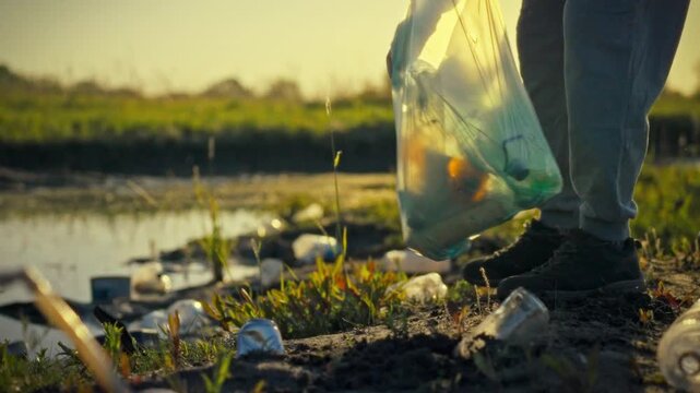An environmental volunteer's hands sort plastic waste from glass trash during an evening cleanup in a natural ecosystem, supporting sustainability and conservation efforts to protect nature