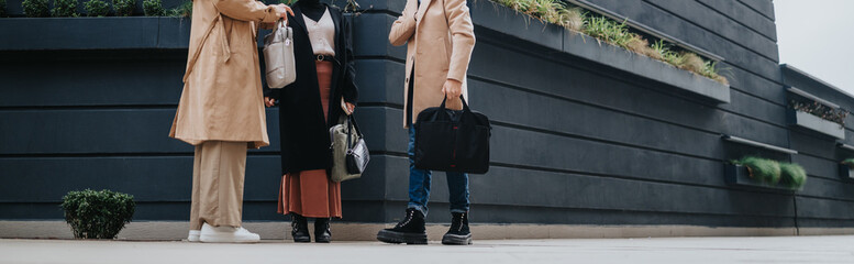 Three colleagues stand on a city sidewalk with briefcases and bags during a casual business...
