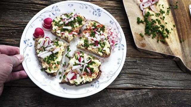 Person places a plate of healthy sandwiches with egg spread, radish, and chives on a table