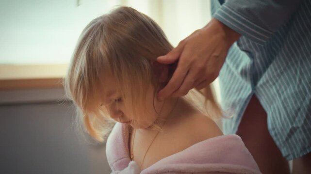 Mother tenderly works out knots her little girl's tangled hair with comb, skillfully transforming it into two adorable ponytails, radiating joy love as girl's face lights up with sweet smile delight