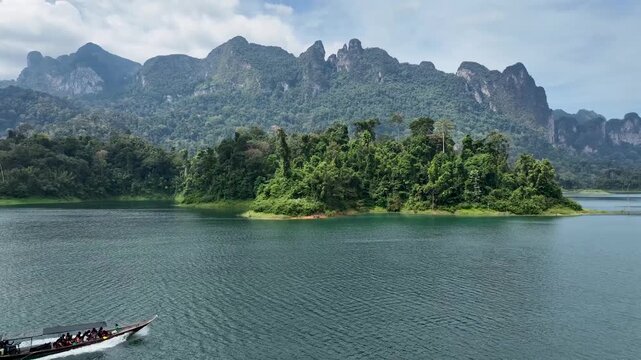 Aerial view of the serene lake surrounded by lush green forest and towering mountains under a cloudy sky, Khao Sok, Surat Thani, Thailand.