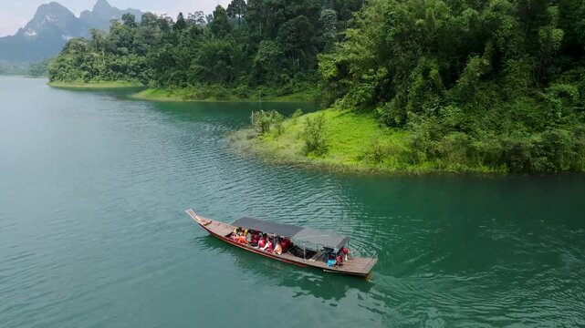 Aerial view of a boat carrying people on a lake, contrasting the dark boat with the green water and lush green shoreline, Khao Sok, Surat Thani, Thailand.