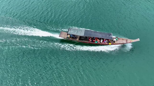 Aerial view of longtail boat slicing through the turquoise waters of the lake, leaving a trail of white foam in its wake, Khao Sok, Surat Thani, Thailand.