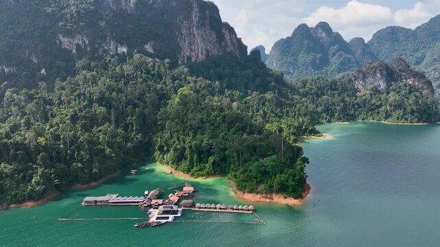 Aerial view of a floating resort contrasts against the backdrop of towering limestone cliffs and lush rainforest, Khao Sok, Surat Thani, Thailand.