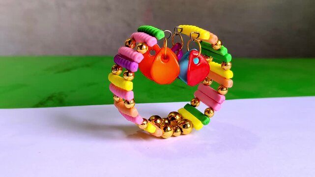 Handmade colorful beaded bracelet with gold accents and heart charms on a bright background.vibrant, multi-colored handmade elastic bracelet featuring flat polymer clay beads, shiny gold spherical bea