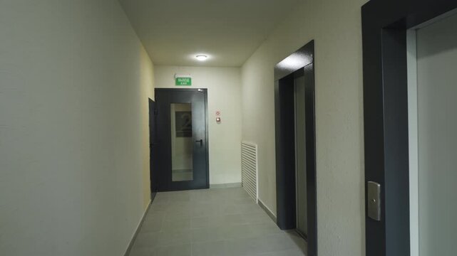 Residential corridor with elevators and floor number sign leading toward exit door. Hallway interior inside modern apartment building