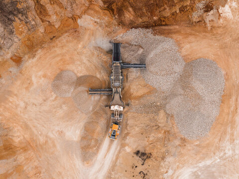 Aerial view of a vast quarry where heavy machinery contrasts against the stark, textured earth, a scene of industrial activity etched into the landscape, Arsoli, Lazio, Italy.