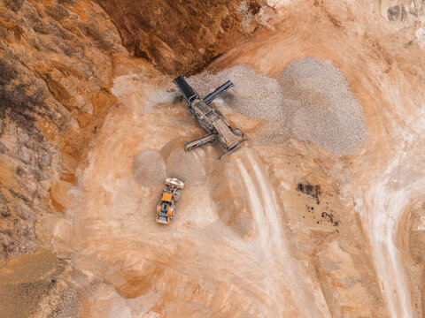 Aerial view of heavy machinery amidst the stark, contrasting textures of a quarry, where beige earth meets piles of grey gravel, Arsoli, Lazio, Italy.