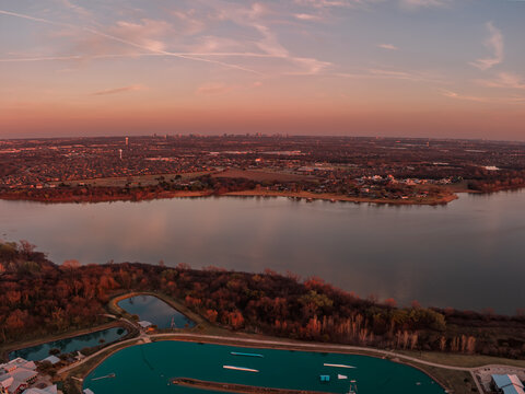 Aerial view of a serene lake reflecting the vibrant sunset sky, with the city skyline softly silhouetted in the distance, Little Elm, United States.