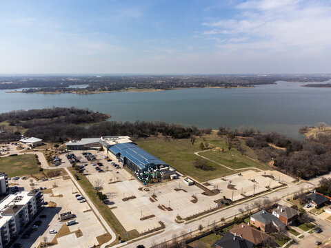 Aerial view of a large building with blue roof contrasts against the vast lake in the distance, Little Elm, Texas, United States.