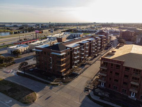 Aerial view of sun-kissed apartment buildings casting long shadows on the asphalt streets, juxtaposed against the distant highway and urban sprawl, The Colony, Texas, United States.