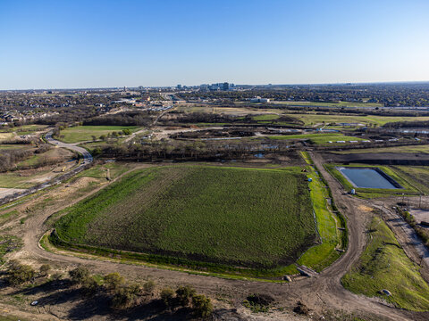 Aerial view of a patchwork of green fields and water bodies contrasting with the distant urban skyline, Frisco, United States.