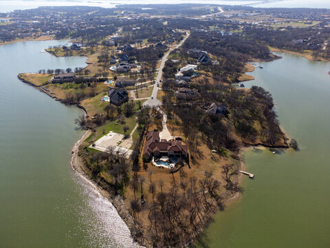 Aerial view of houses and roads on a peninsula surrounded by water, with the landscape in muted earth tones contrasting with the water's reflective surface, Little Elm, Texas, United States.