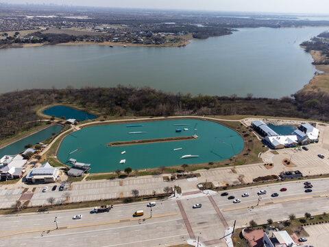 Aerial view of a vibrant wakeboarding park with its crystal-clear waters contrasting against the surrounding green landscape, Little Elm, Texas, United States.