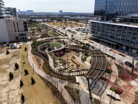 Aerial view of a meticulously designed park with winding paths and modern structures, a verdant oasis nestled amid towering buildings, Frisco, USA.