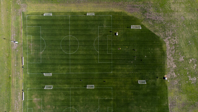 Aerial view of neatly lined soccer fields with bright green grass sharply contrasted by darker shaded areas, Frisco, Texas, United States.