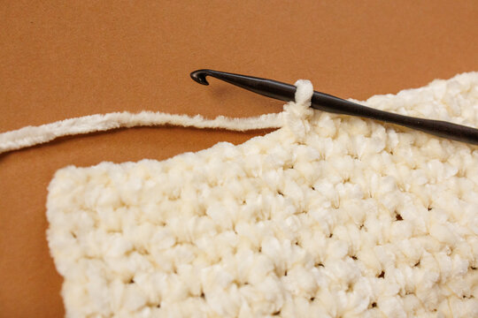 Crochet fabric square with hook and yarn on brown background