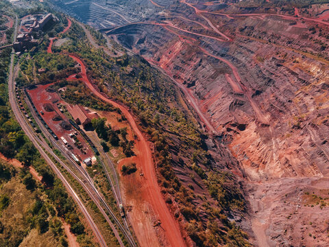 Aerial view of the stark red earth contrasting with the green foliage beside railway tracks near industrial structures and a vast quarry, Kryvyi Rih, Dnipropetrovsk Oblast, Ukraine.